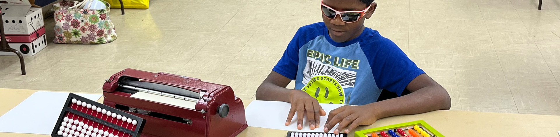 A young boy smiles as he reads from a Braille page during a Connecticut BELL Academy.